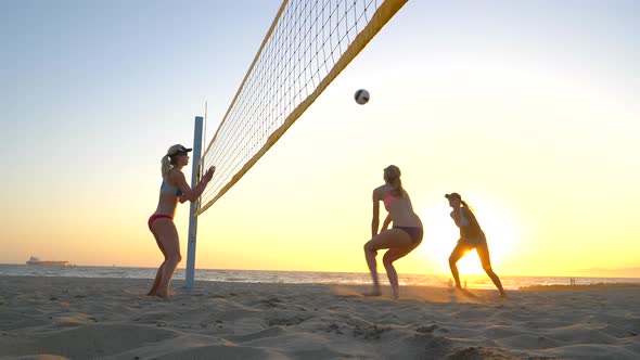 Women players play beach volleyball and a player hitting spiking the ball.