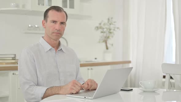 Serious Middle Aged Man with Laptop Looking at the Camera