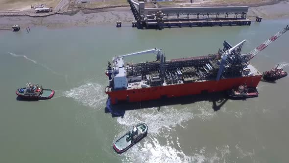 Aerial view of cargo ship arriving at the port with the help of tugs.