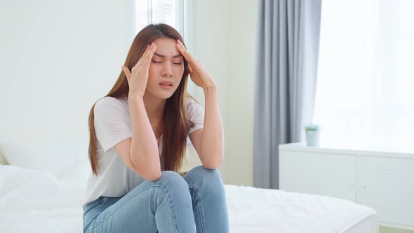 Unhappy young woman touching forehead with fever and migraine headache in the morning at home.