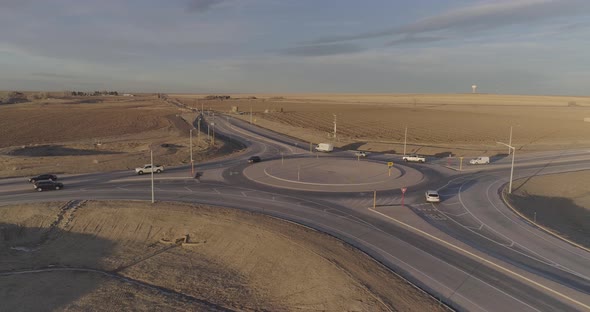 Cars and farm trucks navigate a modern roundabout far from the city.