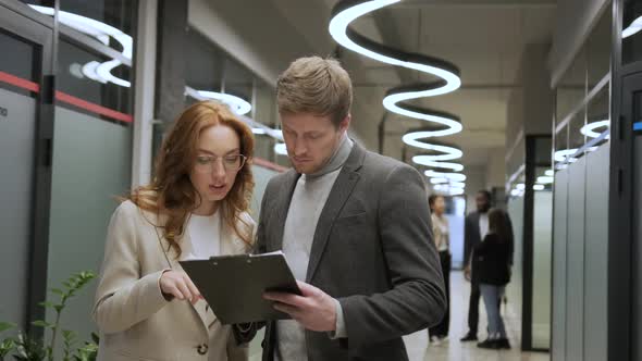 Concentrated Male and Female Employees are Standing in Office Hall Looking at the Tablet