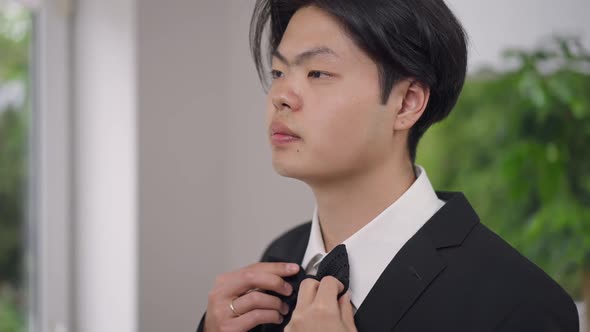 Closeup Portrait of Happy Asian Young Groom Trying on Bow Tie Turning to Camera Smiling