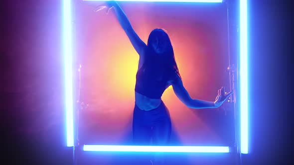 Woman Performs Flexible Movements with Her Hands in Glowing Neon Frame on Orange Smoke Background