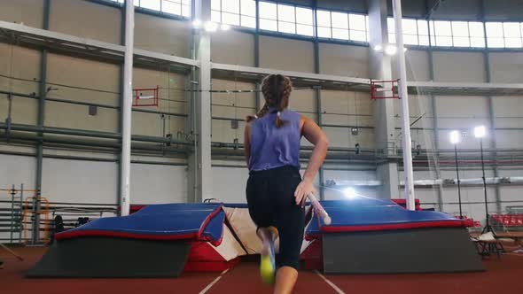 Pole Vaulting in the Indoors Stadium - Young Woman with Pigtails Jumping Over the Bar and Falling