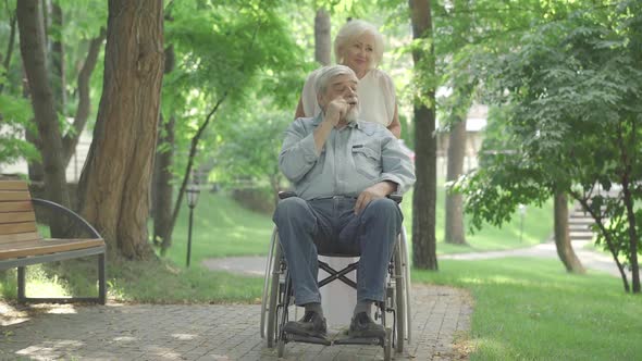 Wide Shot of Positive Beautiful Caucasian Senior Woman Rolling Wheelchair with Disabled Man in