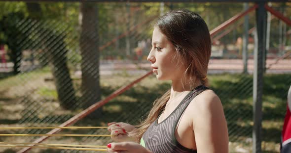 Sporty Woman with Personal Trainer Doing Exercises with Resistance Band Outside