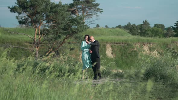 Wide Shot Portrait of Happy Adult Elegant Couple Standing in Sunshine on Windy Day Outdoors Pointing