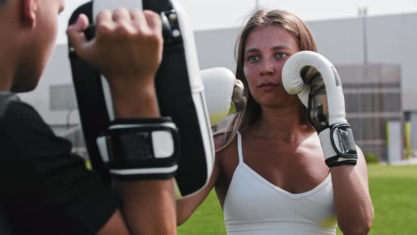 Young Woman in Boxer Gloves Punching in Mitts on the Hand of Her Male Trainer