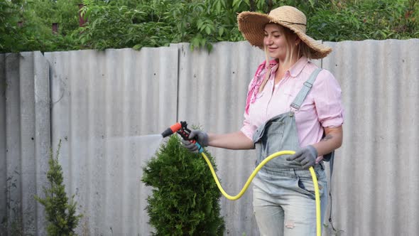 A Young Adult Woman Wateres a Vegetable Garden with a Garden Hose Outside the House