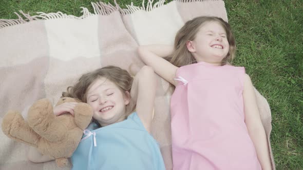 Top View of Happy Laughing Twins Lying on Blanket Outdoors. Portrait of Happy Relaxed Caucasian