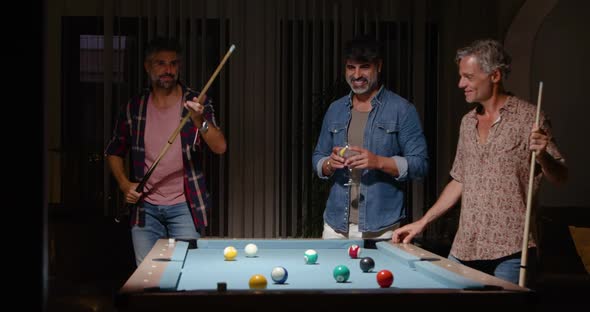 Cheerful men playing billiard while spending time together