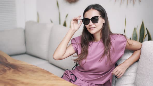 Portrait of Beautiful Woman in Dark Sunglasses Sits in Cafe, Looking at Camera