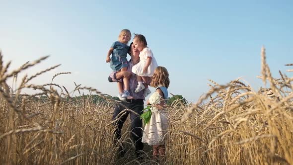 man wheat field holds girls on his shoulders throws them up and children laugh