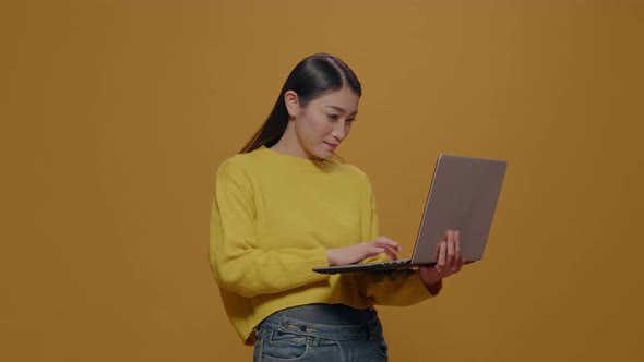 Asian Woman Using Laptop in Front of Camera Over Yellow Background