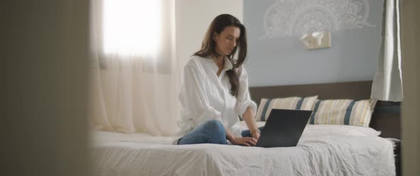 A young woman sitting in bed with laptop, working from home