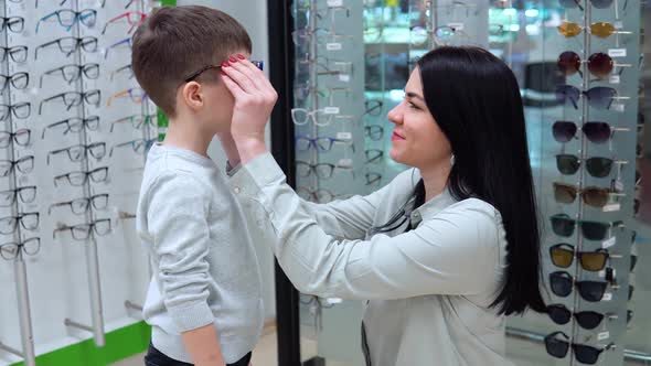 Young Caucasian Woman with Baby Mother and Son Choosing Glasses in Optics Store