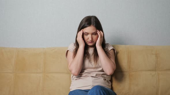 Young Woman Suffering From Headache While Sitting on Sofa