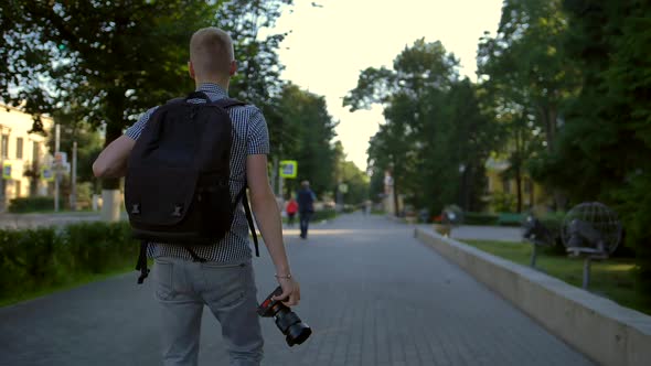 A Student Photographer Is Walking Along a City Street Behind Him