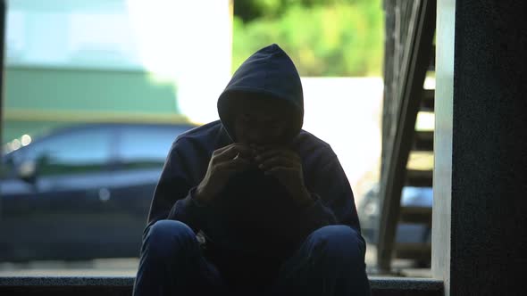 Homeless Hungry Guy Eating Sandwich Sitting in Darkness on Stairs, Crisis