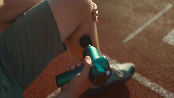 A Male Athlete Massages Muscles and Tendons with a Massage Percussion Device After a Workout at the