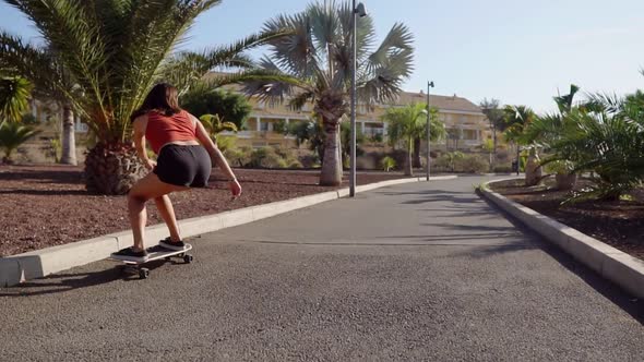 Young Girl Rides on Road Near Palm Trees on Longboard in Slow Motion