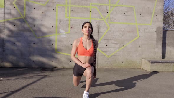 Young Latina woman doing forward lunges outdoors, Front View