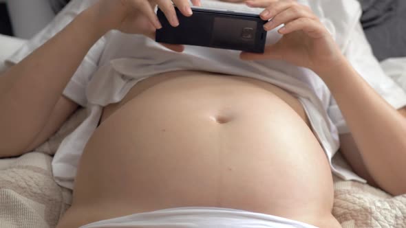 Pregnant Woman with Bare Belly Resting at Home and Using Cellphone
