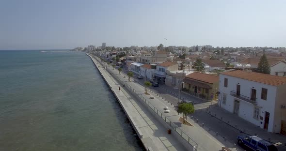 Drone aerial view of pedestrians walking the boardwalk and cars driving along the coast of Larnaca i