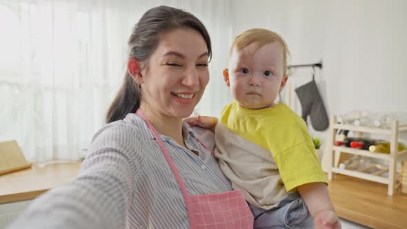 Caucasian mother holding little baby and video call online with family using mobile cellphone.