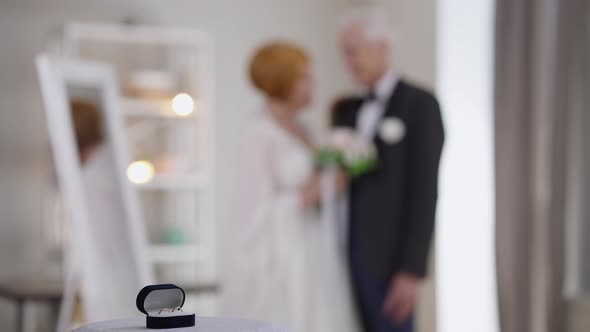 Two Wedding Rings in Box and Blurred Caucasian Senior Couple Standing at Background