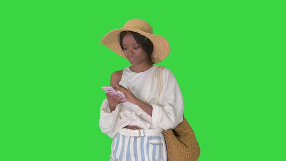 Smiling Young African American Woman in a Straw Hat Texting on Her Phone on a Green Screen, Chroma