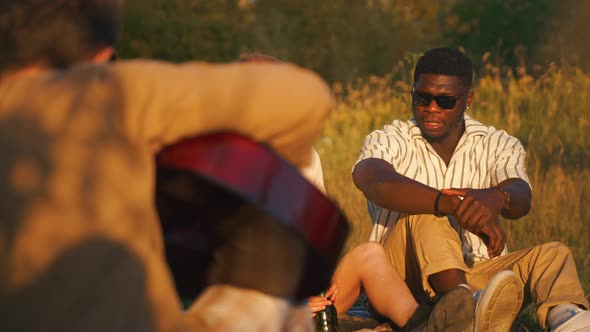 Group of Happy Young People Having a Weekend Picnic in Nature Sitting Together on the Grass Near the