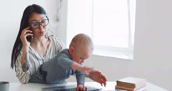 Young Mother Freelancer with Her Child Working at Home Office Using Laptop