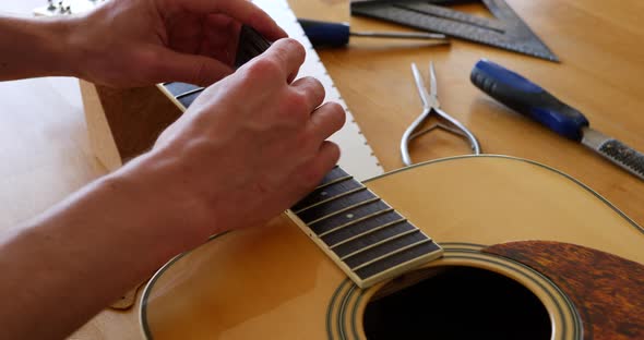 Hands of a luthier craftsman measuring and leveling an acoustic guitar neck fretboard on a wood work