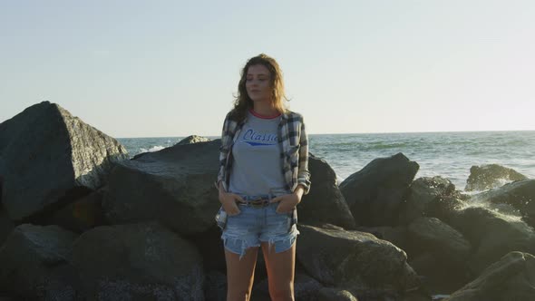 Girl standing by the breakwater rocks near the ocean alt