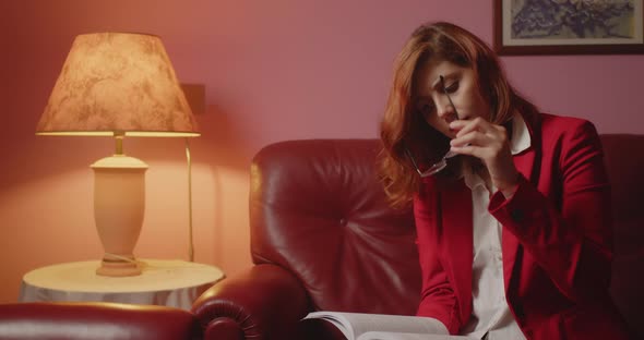 Girl does not see the book well and puts on her eyeglasses while reading sitting on the sofa