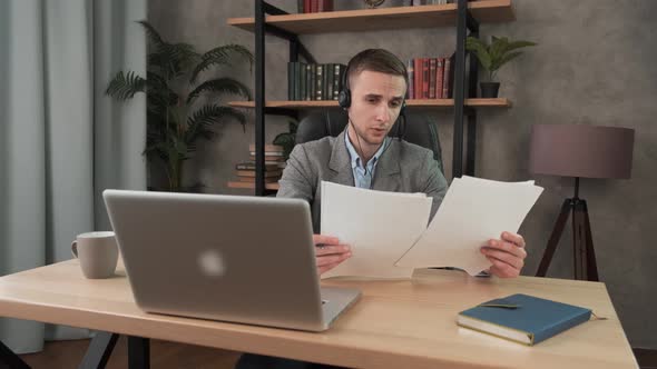 Young Smiling Man Employee Doing Paperwork in the Office at the Computer. Male Worker Looking with