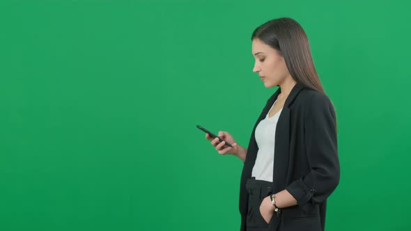 Attractive European Businesswoman in Suit Is Using a Smartphone on Chromakey Green Screen Background