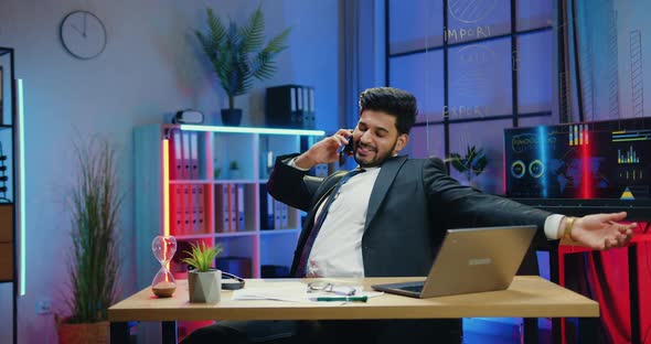 Businessman in Suit Has Pleasant Phone Conversation while Ovetime Working in Evening Office