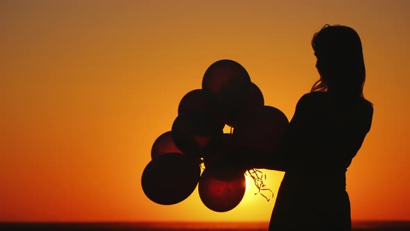 Silhouette of a Young Woman with Balloons at Sunset