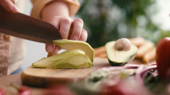 Close up of hands of woman cutting avocado at the kitchen