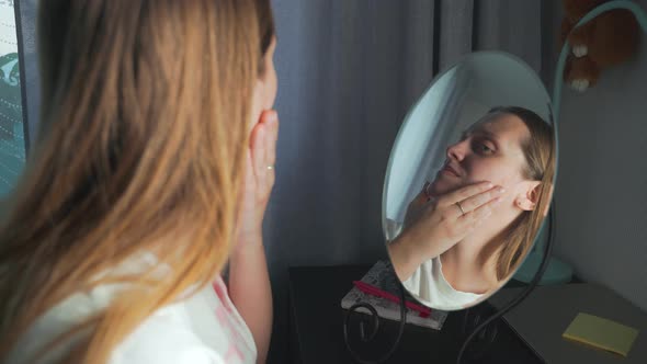 Young Woman Looks at Herself in the Mirror Examines the Skin of Her Face and Gets Upset