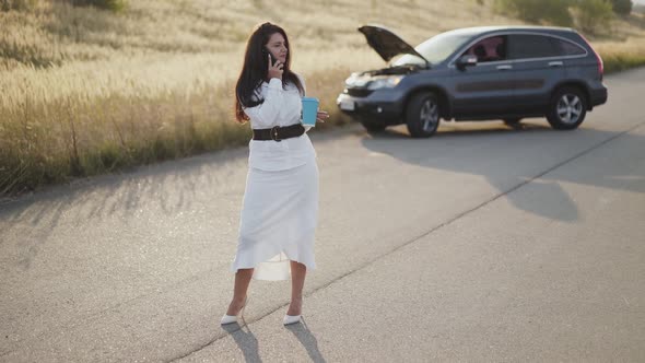 Business Woman Holds a Cup of Tea and Talks on Phone at Broken Car Out of City