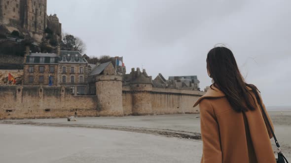 Camera Follows Beautiful Happy Tourist Woman Walking Close To Epic Mont Saint Michel Castle on