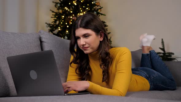 Woman Uses Laptop Online Chatting with Friends on Background Christmas Tree