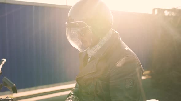 Motorcyclist Sits on an Old Caferacer Motorcycle Harbor Background