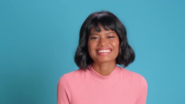Happy Young Woman Smiles Broadly at Camera Against Blue Background