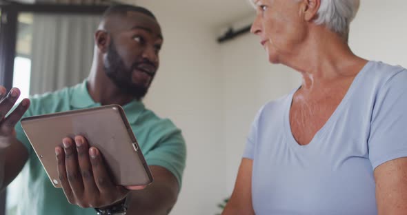 Video of african american male physiotherapist using tablet with caucasian senior woman