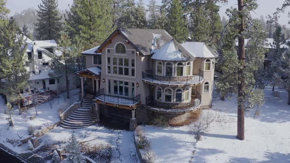 Warm Christmas welcome home winter Big Bear California aerial, Snow Covered Mansion surrounded by tr